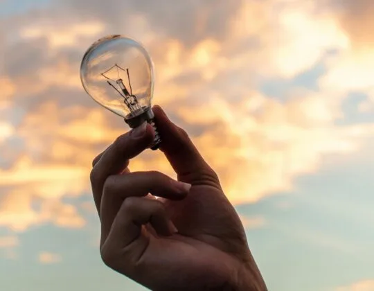 En hand håller upp en glödlampa mot himlen
